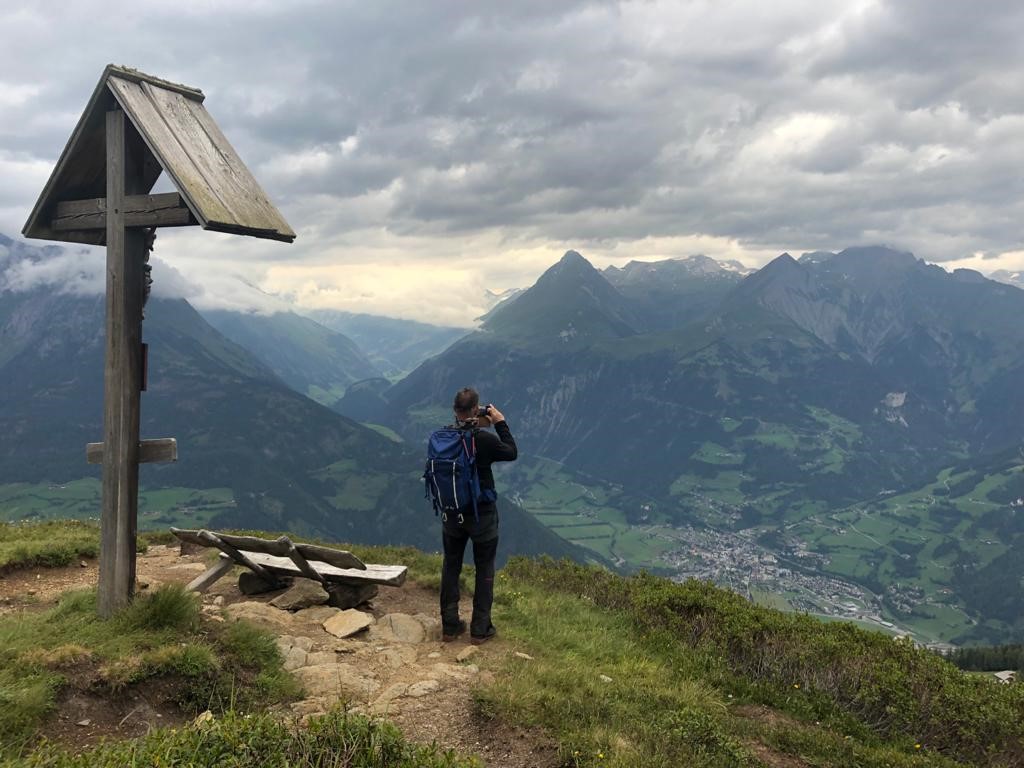 Mann steht auf Gipfel und macht Foto von der Bergkulisse