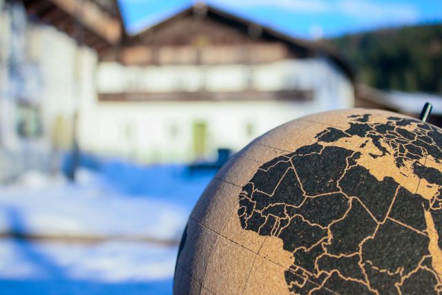 IM Vordergrund ein Globus aus Kork und im Hintergrund Bauernhaus