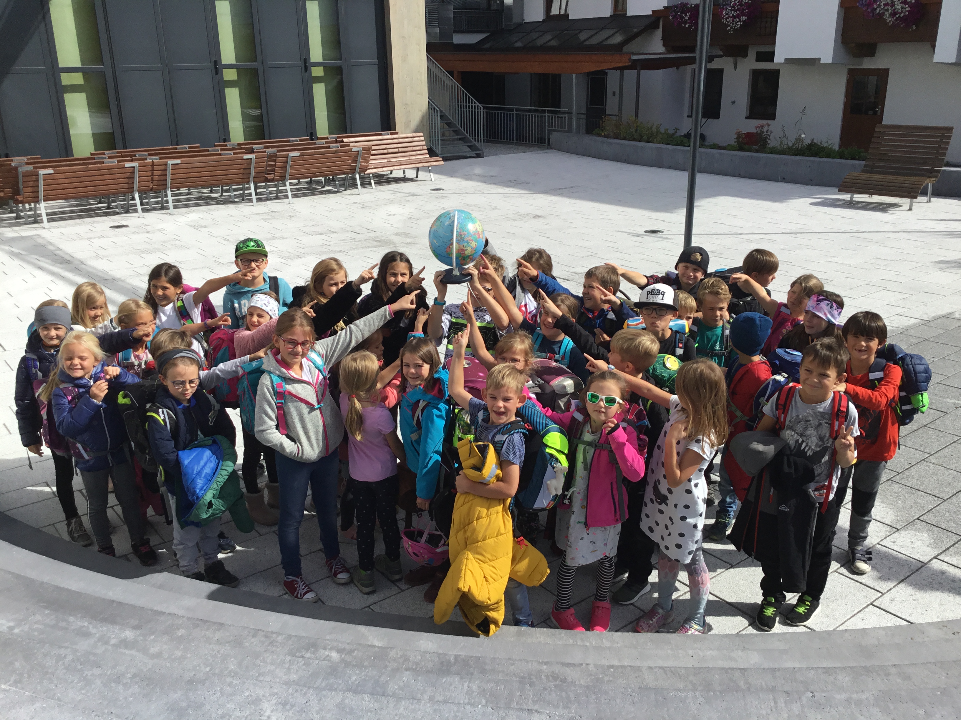Kinder einer Volkschule stehen in der Gruppe zusammen und halten einen Globus gemeinsam in die Luft