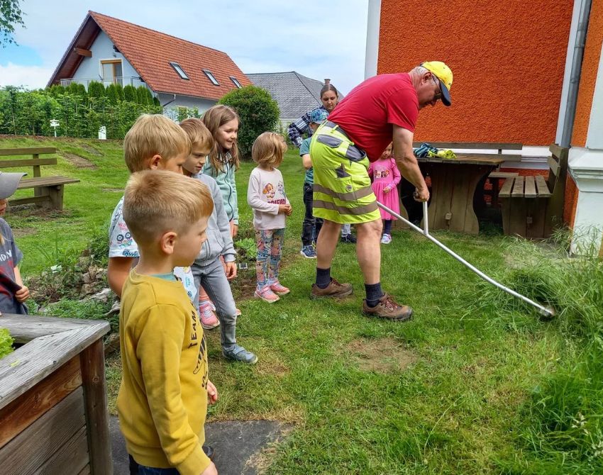 Mann nutzt eine Sense zum Mähen der Wiese, Kinder schauen zu