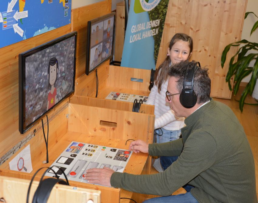 Mann forscht an interaktiver Station und spricht mit Bildschirm zu Kind an einem Ort mit Extremwetter