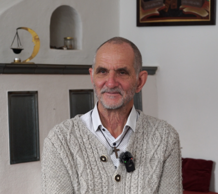 Ein älterer Mann sitzt vor dem Kamin und lächelt in die Kamera