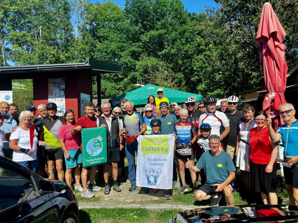 Radlobby-Mitglieder mit Radbekleidung und Helmen, die sich in Österreich vor Bäumen aufstellen.
