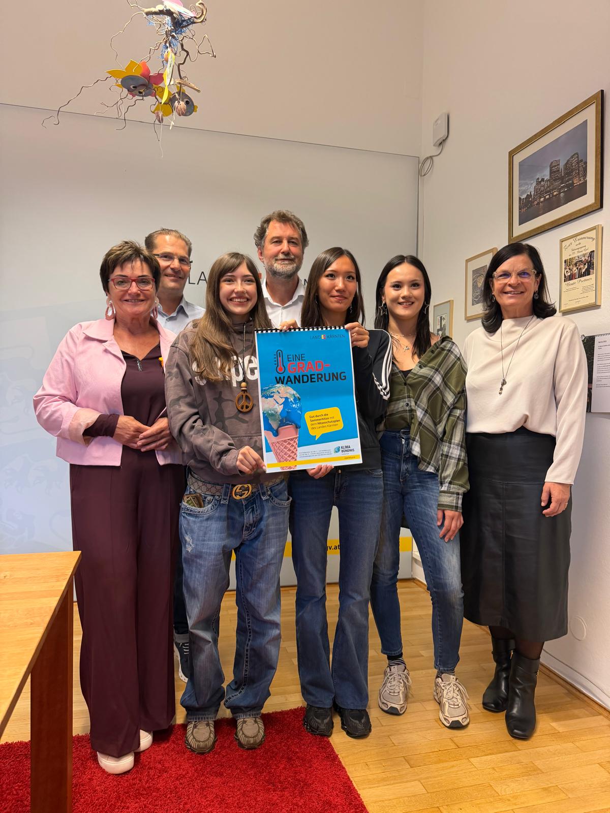 Sieben Personen halten ein Plakat mit dem Titel "Eine Grad Wanderung" in Klagenfurt.