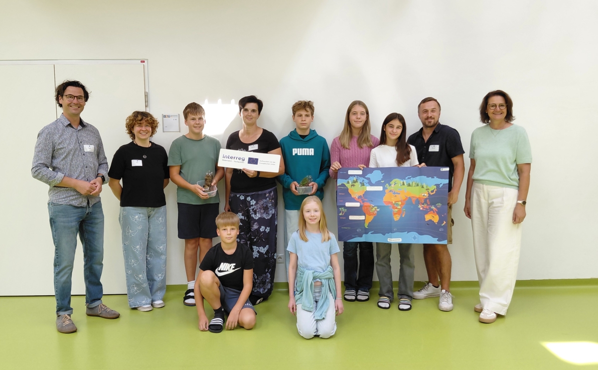 Gruppe von Kindern und Erwachsenen mit einer Weltkarte und Pflanzen vor weißer Wand