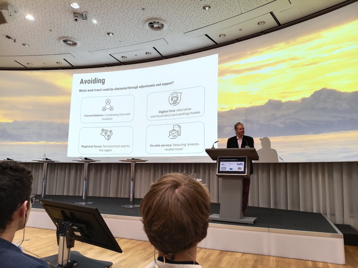 Vortragender am Rednerpult vor einer Leinwand mit Präsentation und Berglandschaft