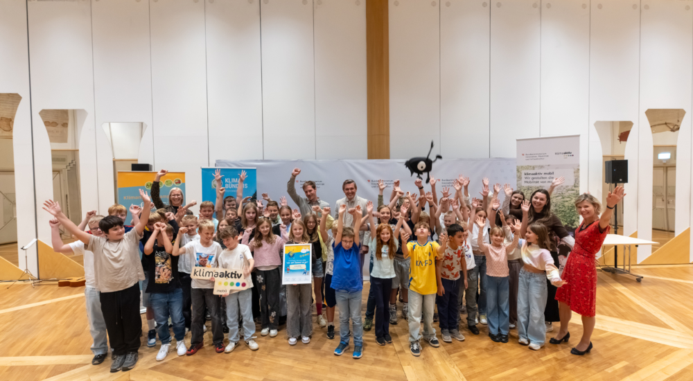 Kinder und Erwachsene mit erhobenen Händen vor einem Banner des Klimabundes in Wien